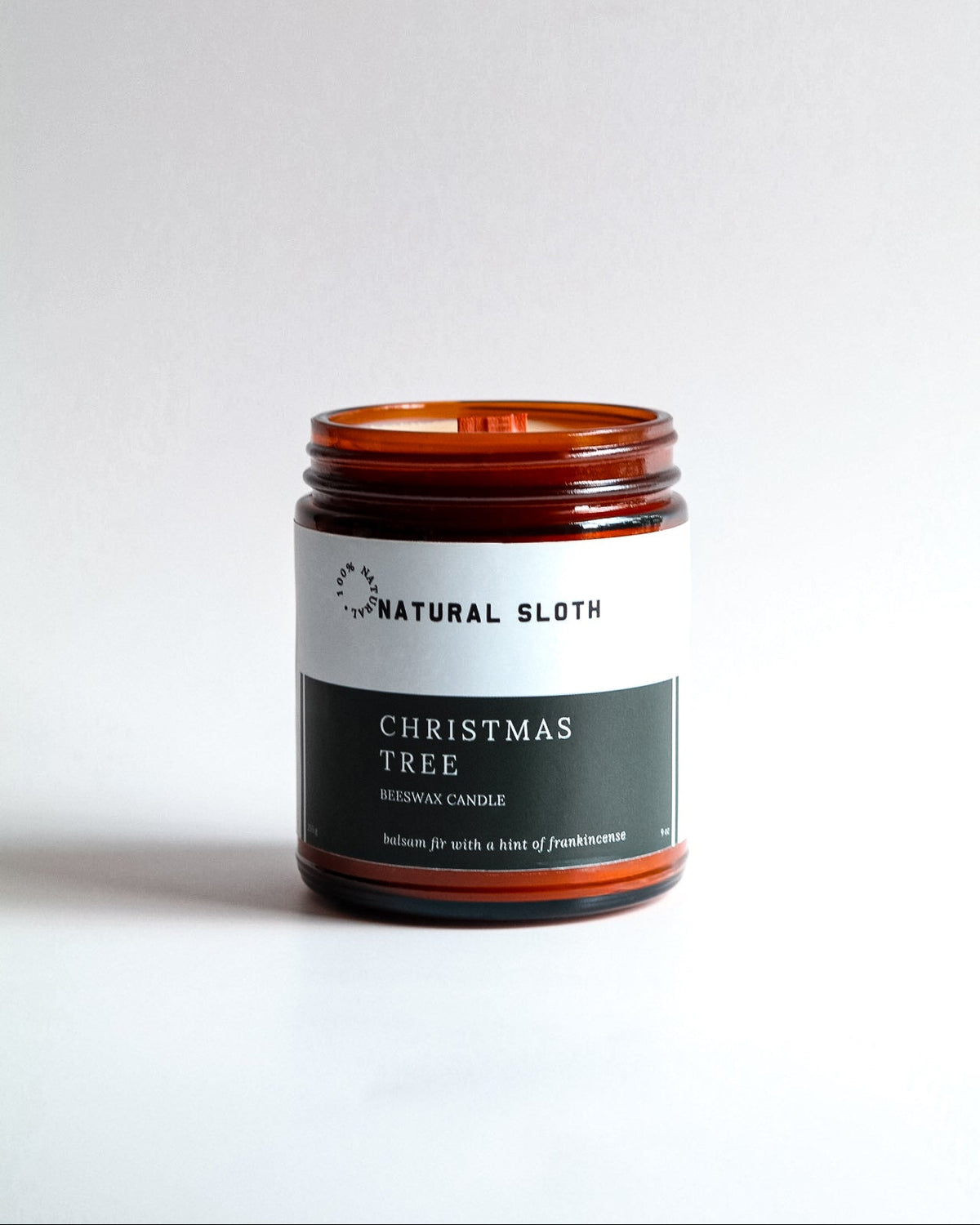 An amber glass jar Beeswax candle with a white and dark green label reading 'Natural Sloth Christmas Tree' on a clean white background.